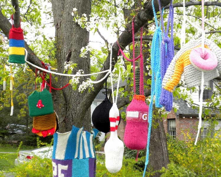 Multiple knitted ornaments hanging from blossoming spring branches