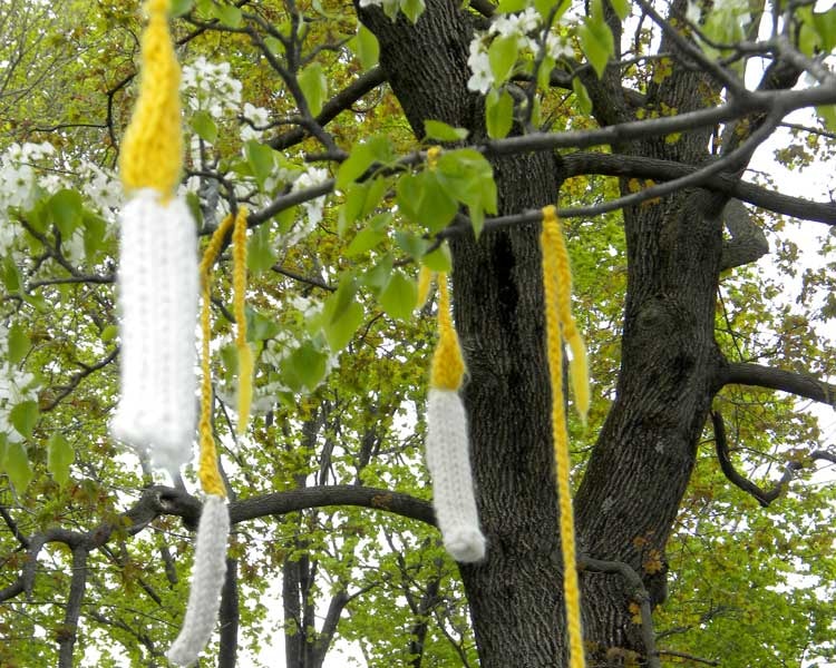 Knitted white candles with yellow flames hanging in the leafy tree