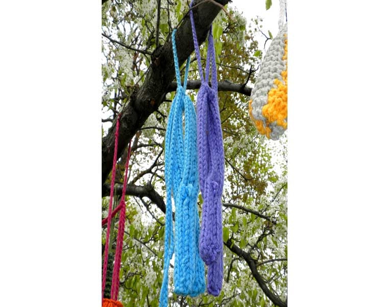 Blue and purple knitted healing ribbons hanging from blossoming branches