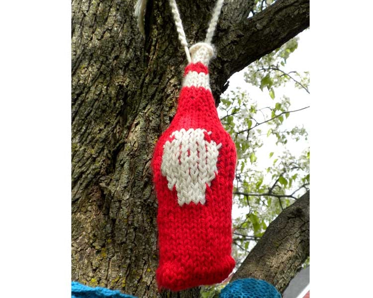 A knitted ketchup bottle hanging from a blossoming branch