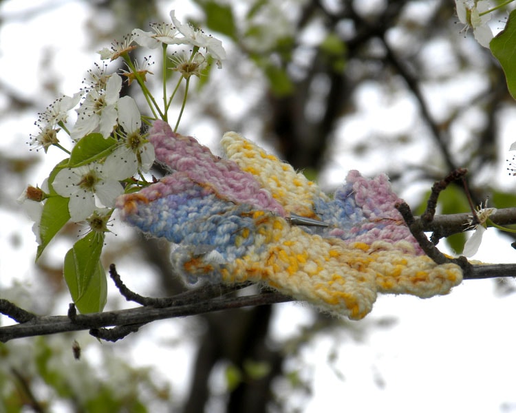A delicate crocheted star shape in soft pastel pink, blue, and yellow, resting on blossoming branches