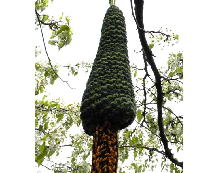 A dark green knitted teardrop or pine-tree shape hanging from a blossoming branch