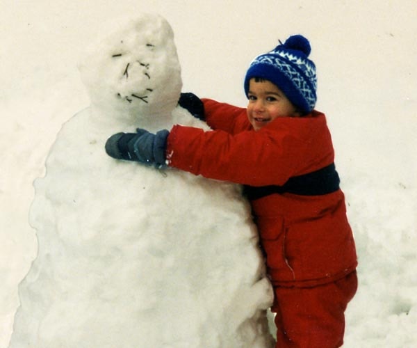 Young Tommy in a red snowsuit hugging a large snowman